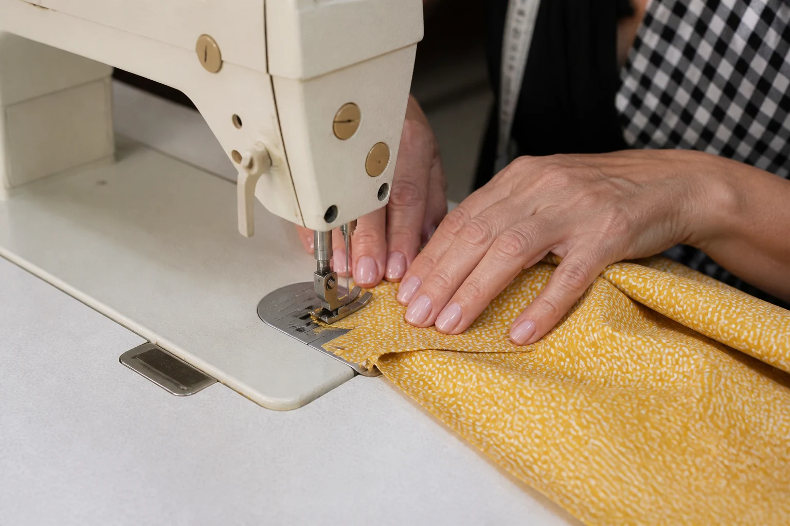 Dikiş makinesinde kumaş işlenirken iğne, baskı ayağı ve ellerin yakın plan görünümü